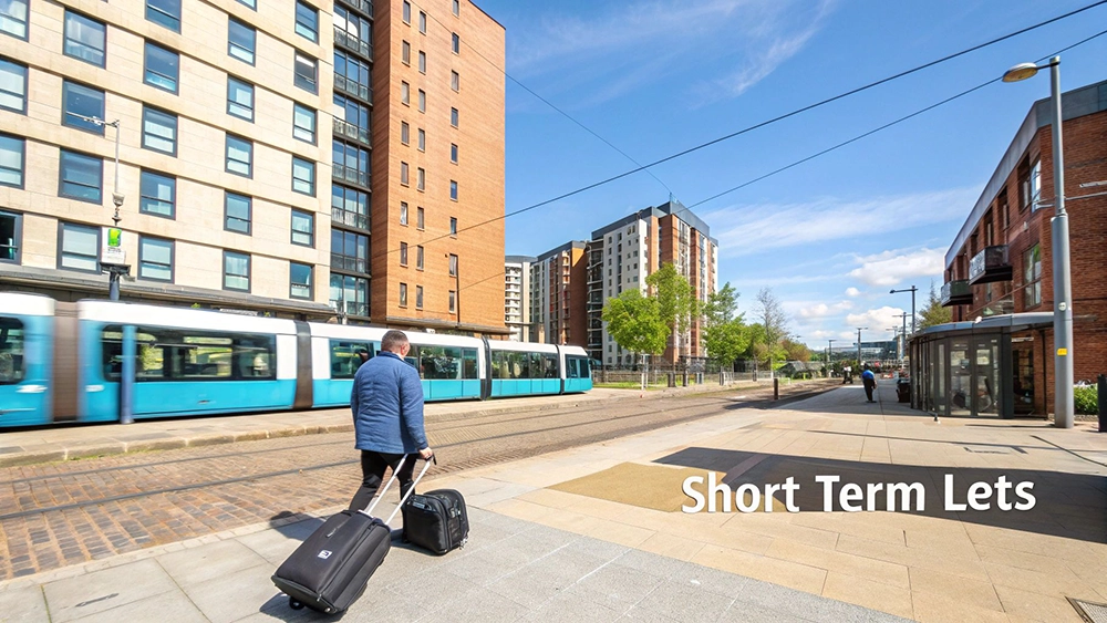 Man with luggage walking past modern apartment buildings and tram in Manchester city center
