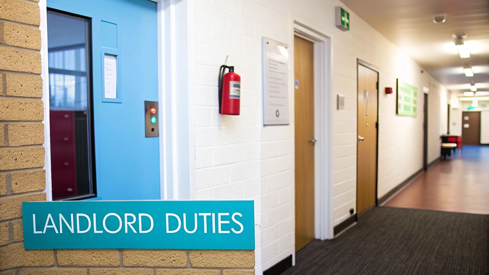 An indoor hallway with an elevator, fire extinguisher, and a prominent 'LANDLORD DUTIES' sign.