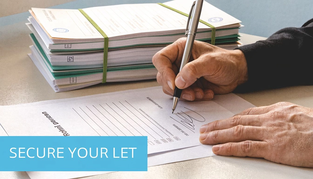 A close-up view of a person's hand signing a rental tenancy agreement document with a pen.